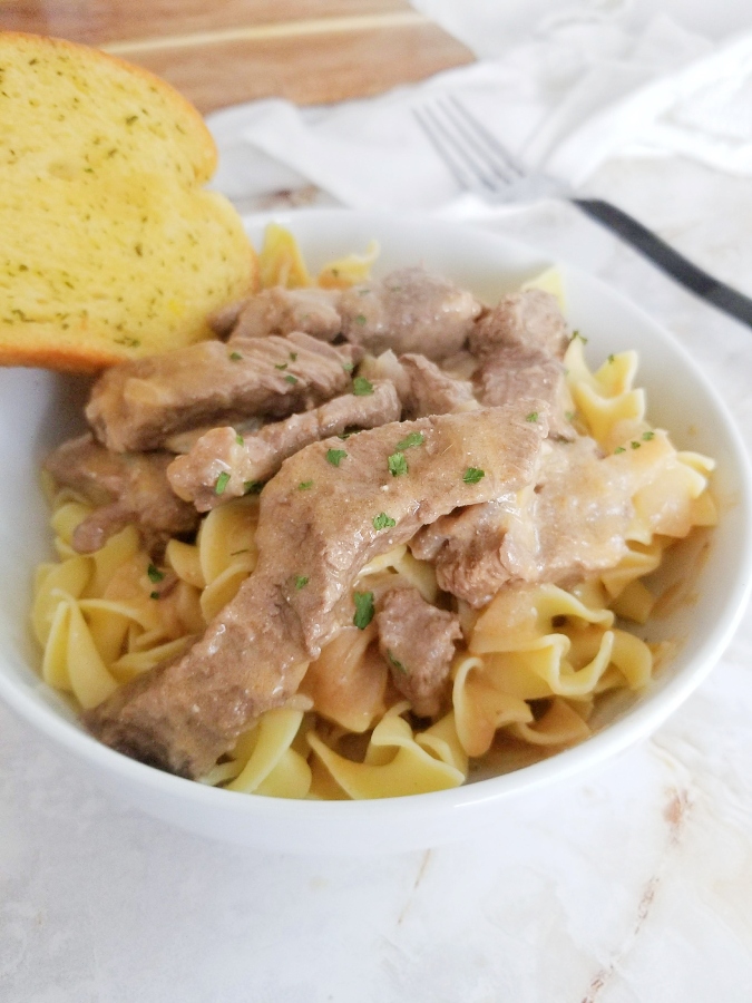 Mom's Beef Stroganoff in white bowl with garlic bread