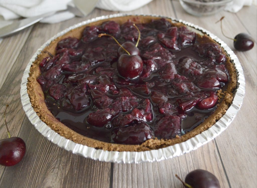 Whole Michigan Chocolate Cherry Tart with cherries against wooden background 