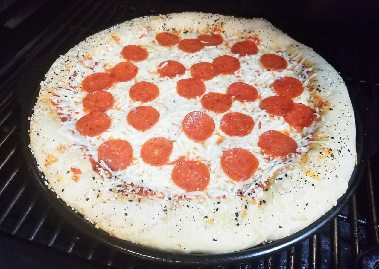 Homemade Pizza Dough cooking with toppings on grill 