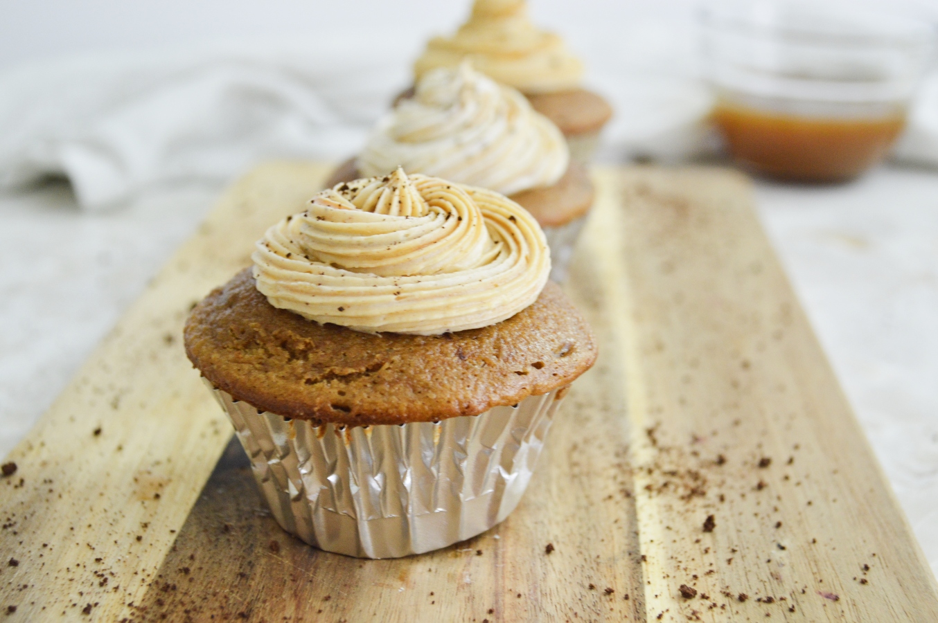 Caramel macchiato cupcakes on wooden board with caramel in background 