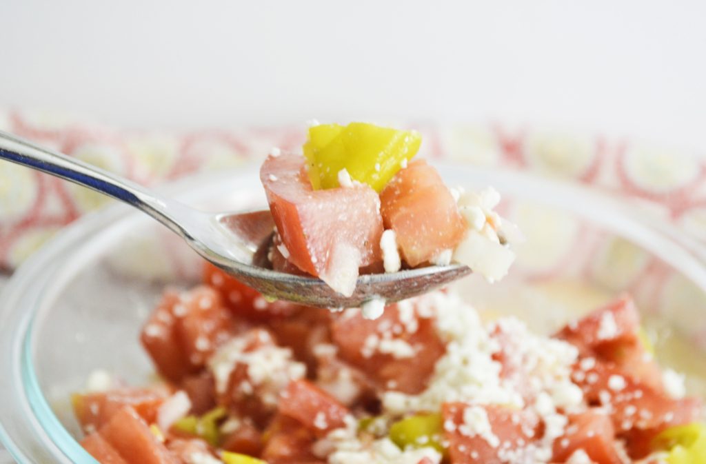 Marinated tomato salad with feta on spoon close up 