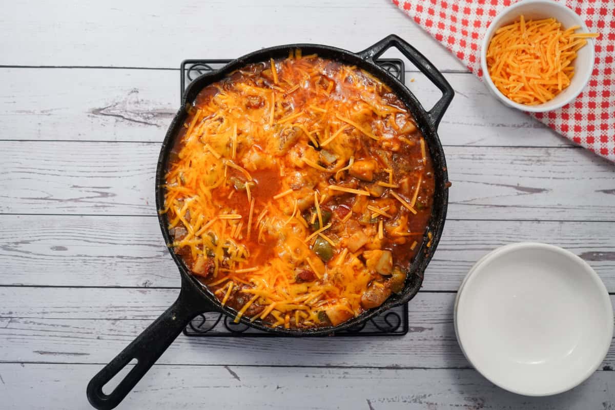 sloppy Joe potatoes in cast iron skillet with bowls and cheese 