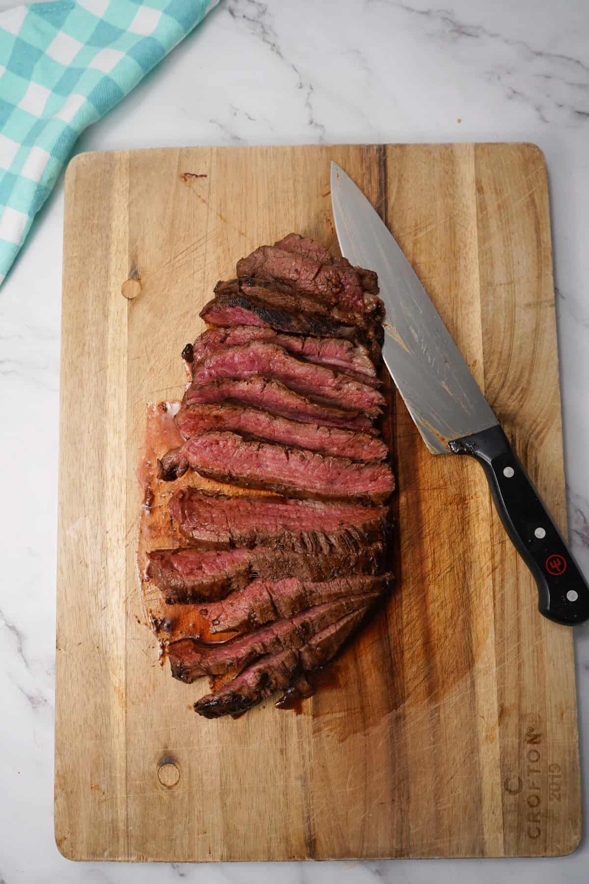 sliced flank steak on brown cutting board with knife