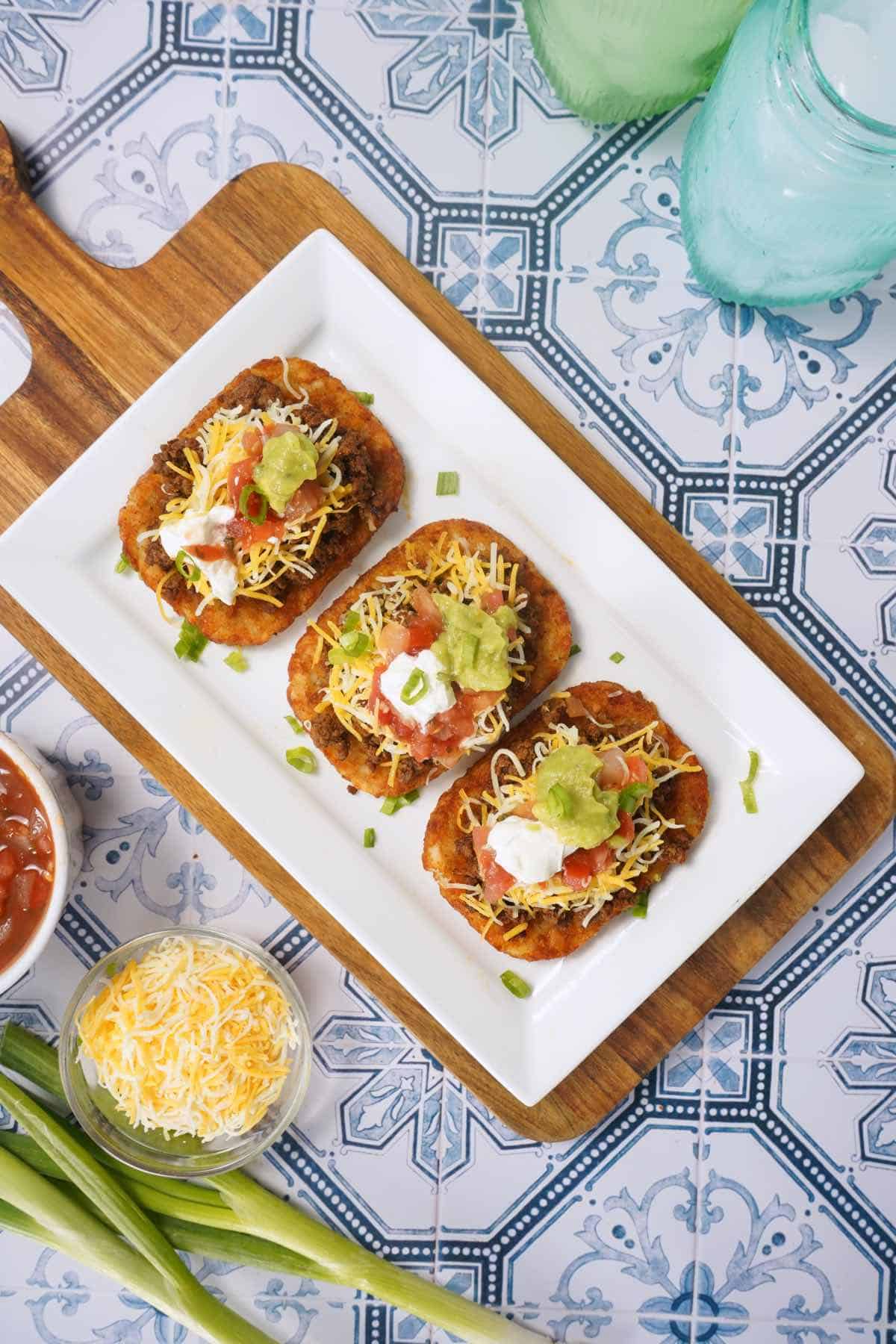 Three loaded hash browns on white plate from above. 