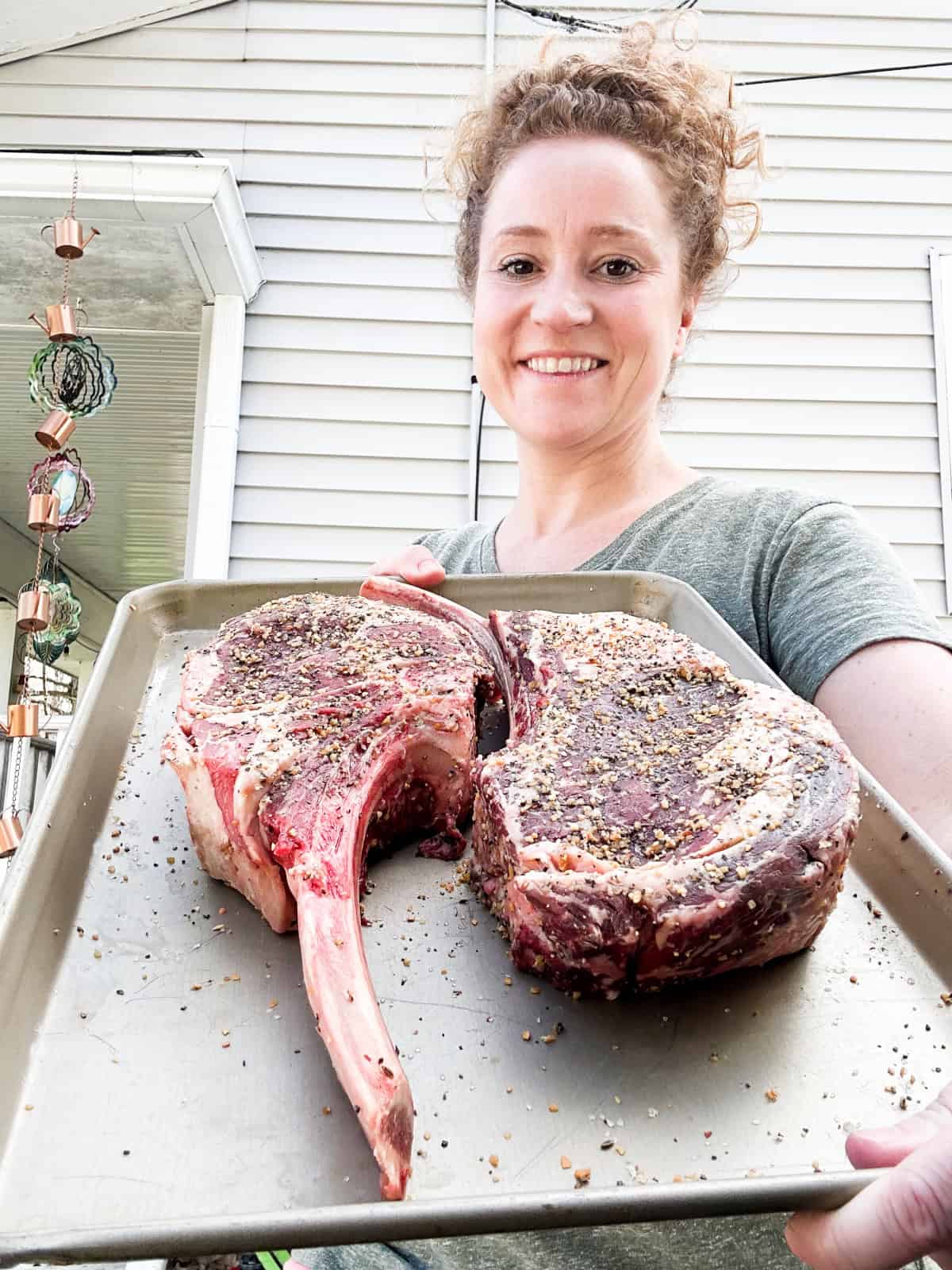 Stef holding sheet pan with Tomahawk steaks before smoking.
