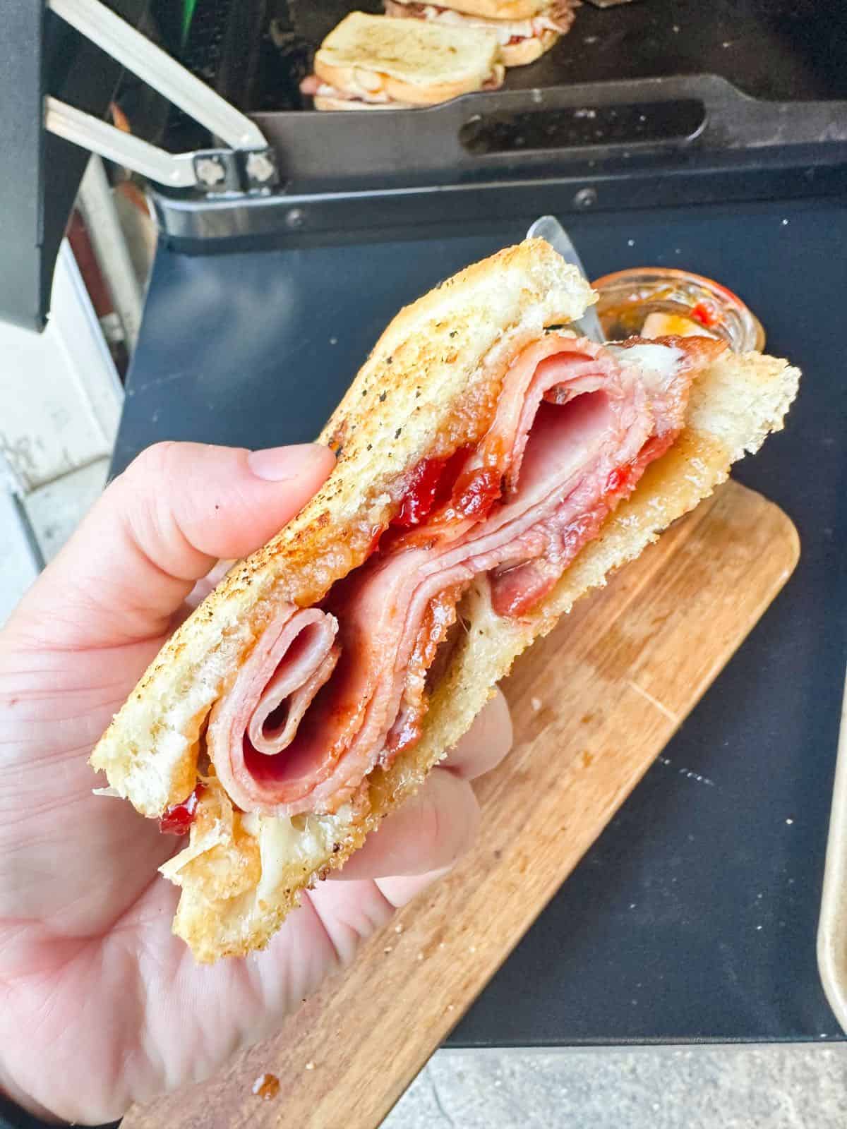 One half of a bacon jam sandwich in hand. 