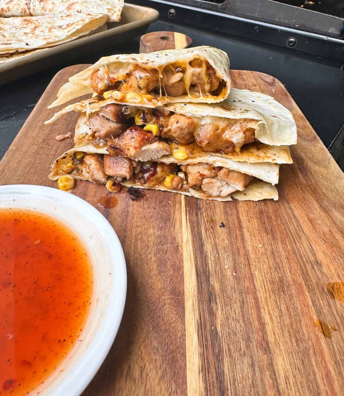 Three bbq chicken quesadillas stacked on cutting board with bbq sauce. 